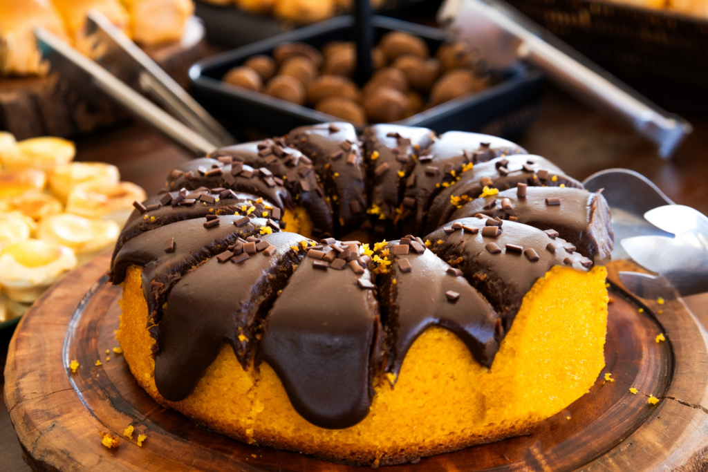 bolo-cobertura-de-chocolate-sobre-tabua-de-madeira-doces-desfocados-ao-fundo